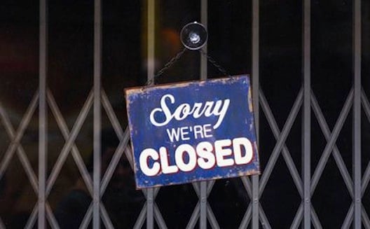Sorry we're Closed sign hanging on a metal gate in front of a buisness.